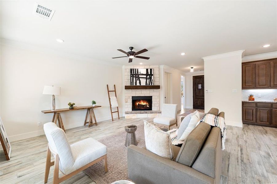 Living room with a fireplace, crown molding, light wood-style floors, recessed lighting, and ceiling fan