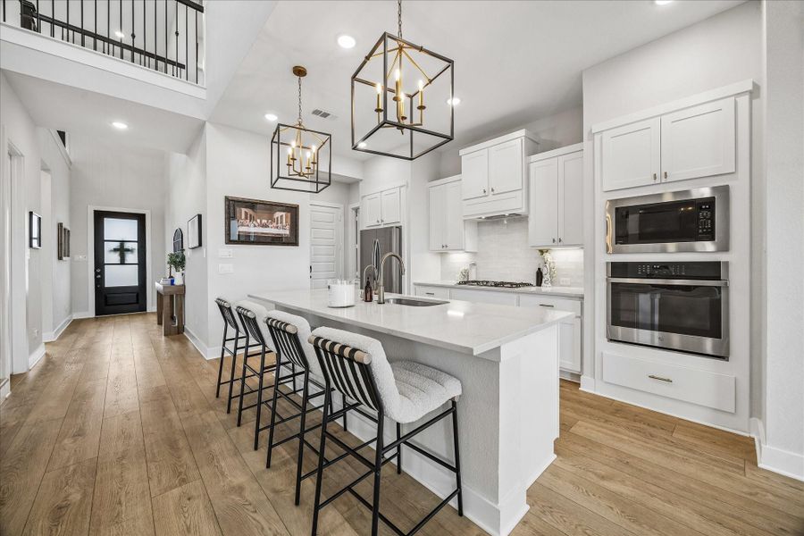 The beautifully designed kitchen features crisp white cabinetry, elegant gold hardware, and stylish pendant lighting above the spacious island with additional seating.