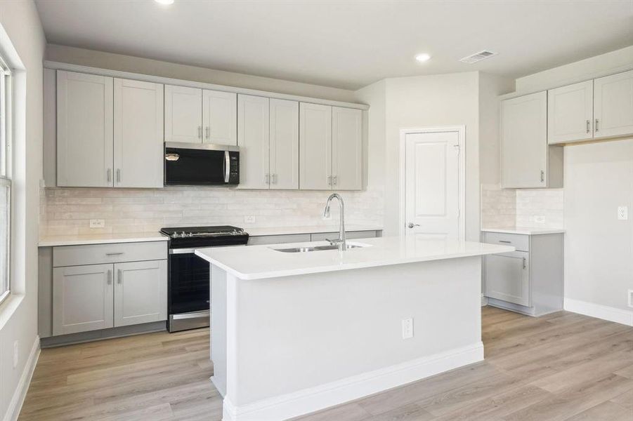 Kitchen featuring appliances with stainless steel finishes, backsplash, an island with sink, light wood-type flooring, and recessed lighting Kitchen featuring appliances with stainless steel finishes, backsplash, an island with sink, light wood-type flooring, and recessed lighting