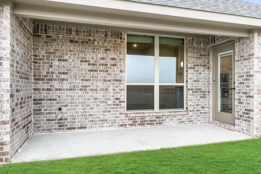 Covered back patio with concrete floor, brick exterior wall, large window, and back door entry