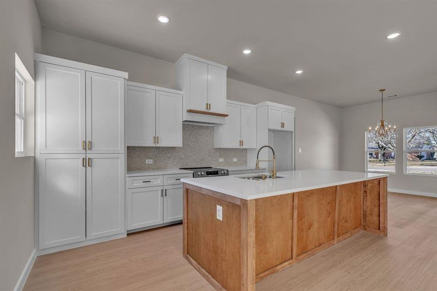 Kitchen with pendant lighting, sink, electric stove, a kitchen island with sink, and white cabinetry