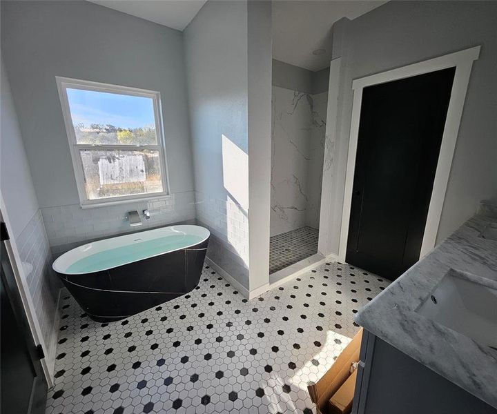 Full bath featuring a freestanding tub, double vanity, a marble finish shower, and tile walls Full bath featuring a freestanding tub, double vanity, a marble finish shower, and tile walls