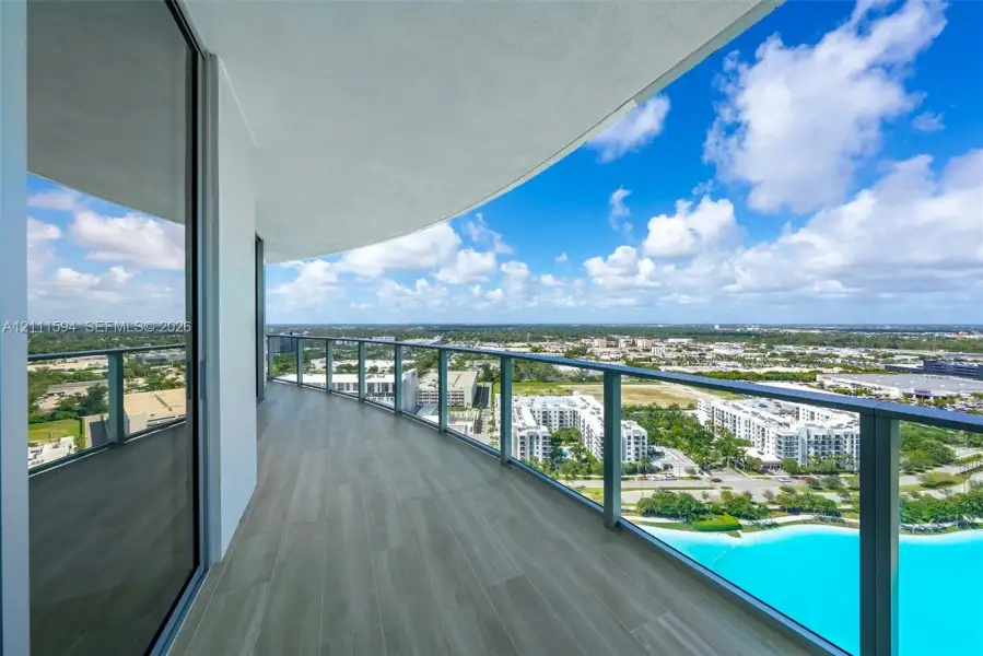 Curved balcony featuring wood-finish tile flooring, a glass panel railing, and expansive exterior scenery Curved balcony featuring wood-finish tile flooring, a glass panel railing, and expansive exterior scenery