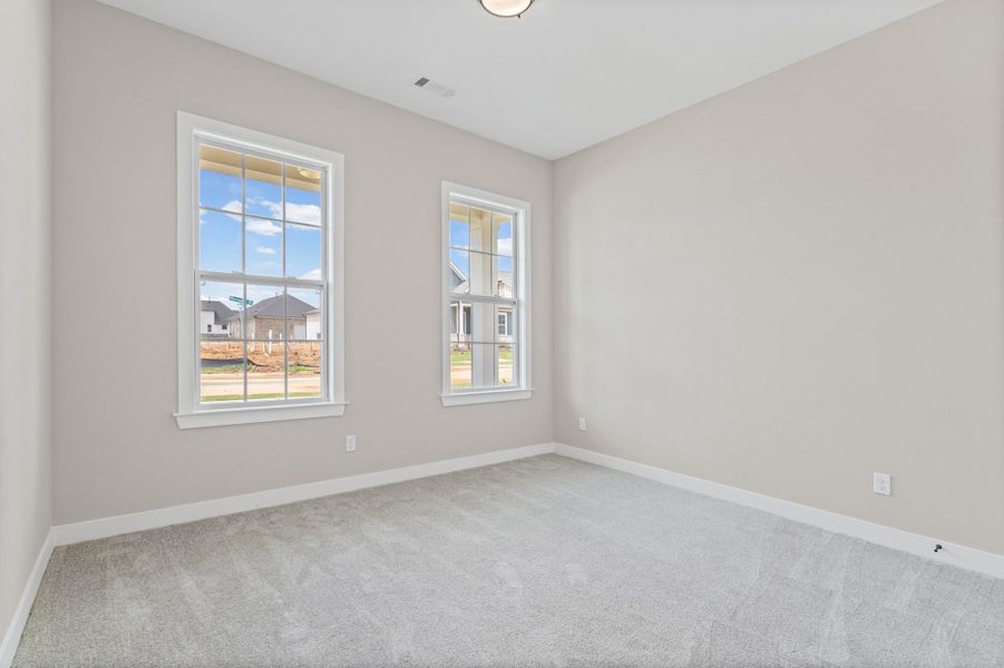 Neutral-toned interior room featuring two large windows, light grey carpeting, white baseboards, and a ceiling-mounted light fixture Neutral-toned interior room featuring two large windows, light grey carpeting, white baseboards, and a ceiling-mounted light fixture