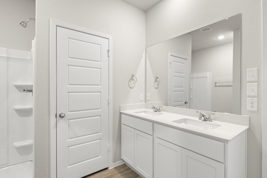 Image of a primary bathroom with light grey walls, a white jack and jill vanity, a large mirror and a white standing shower Image of a primary bathroom with light grey walls, a white jack and jill vanity, a large mirror and a white standing shower