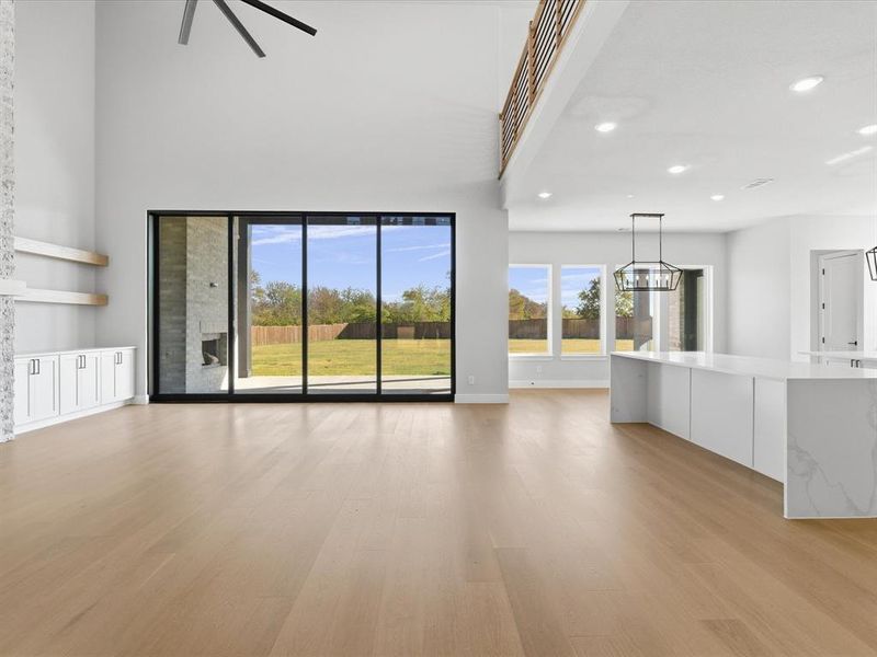 Unfurnished living room featuring light wood finished floors, recessed lighting, a chandelier, ceiling fan, and a towering ceiling