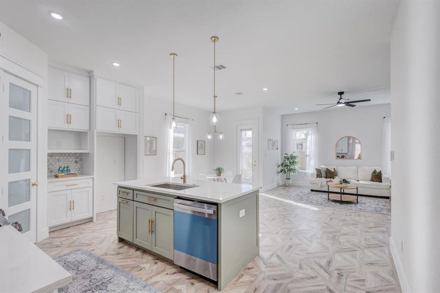 Kitchen featuring sink, decorative light fixtures, a center island with sink, dishwasher, and light parquet flooring