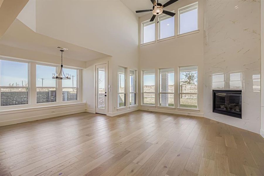 Unfurnished living room with a chandelier, light wood-type flooring, a glass covered fireplace, a towering ceiling, and ceiling fan