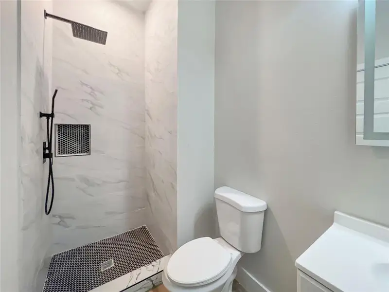 Full bath with toilet, vanity, and a marble finish shower