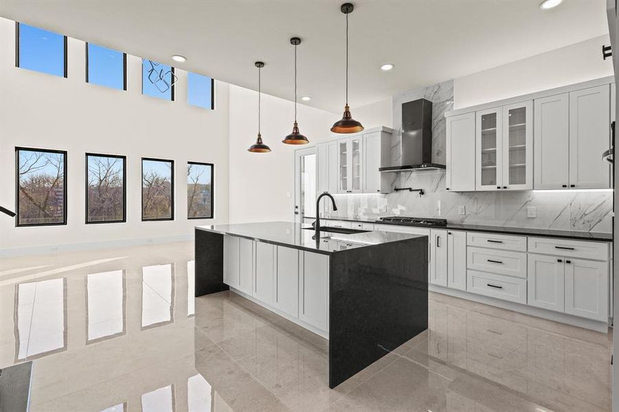 Kitchen with pendant lighting, wall chimney range hood, sink, a center island with sink, and stainless steel gas stovetop