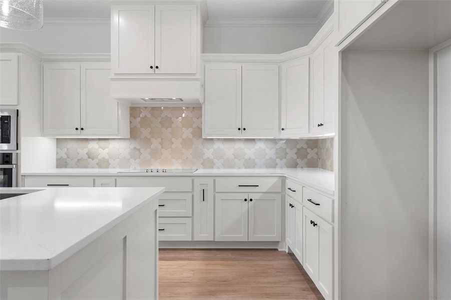 Kitchen featuring white cabinetry, tasteful backsplash, crown molding, light wood-type flooring, and light stone countertops Kitchen featuring white cabinetry, tasteful backsplash, crown molding, light wood-type flooring, and light stone countertops
