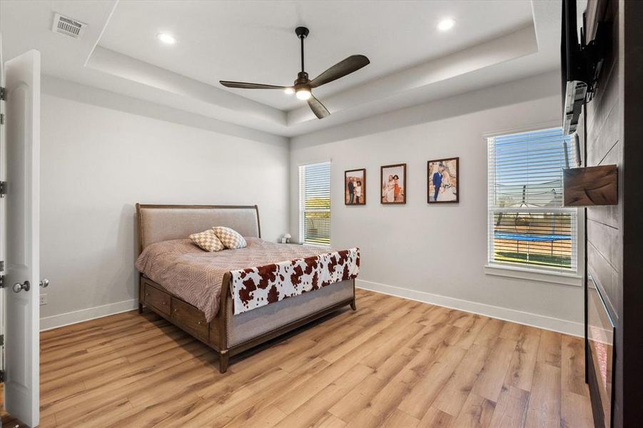Bedroom with a raised ceiling, light wood-style flooring, a ceiling fan, and recessed lighting
