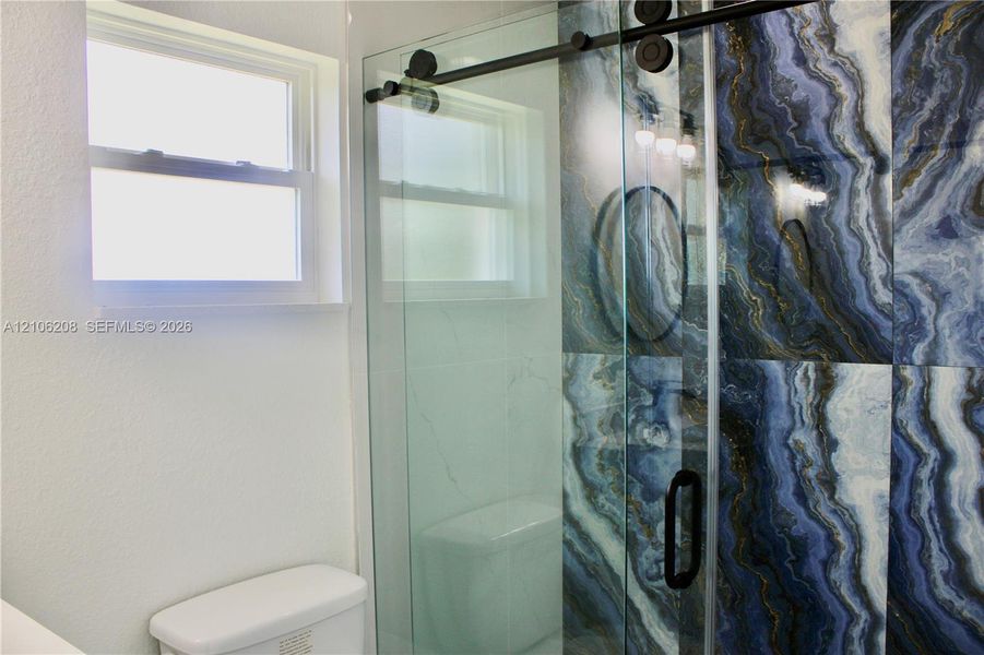 Shower enclosure featuring large-format blue-toned decorative wall tile, sliding frameless glass door with matte black hardware, and single-hung window