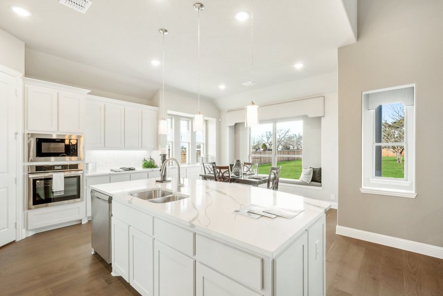 Kitchen with white cabinets, large island with quartz countertop, stainless steel appliances, and pendant lights Kitchen with white cabinets, large island with quartz countertop, stainless steel appliances, and pendant lights