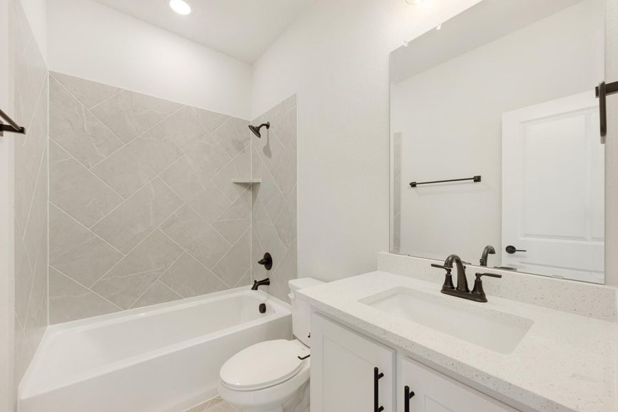 Bathroom with tub-shower combo featuring diagonal gray tile, white vanity with quartz countertop, and dark bronze fixtures