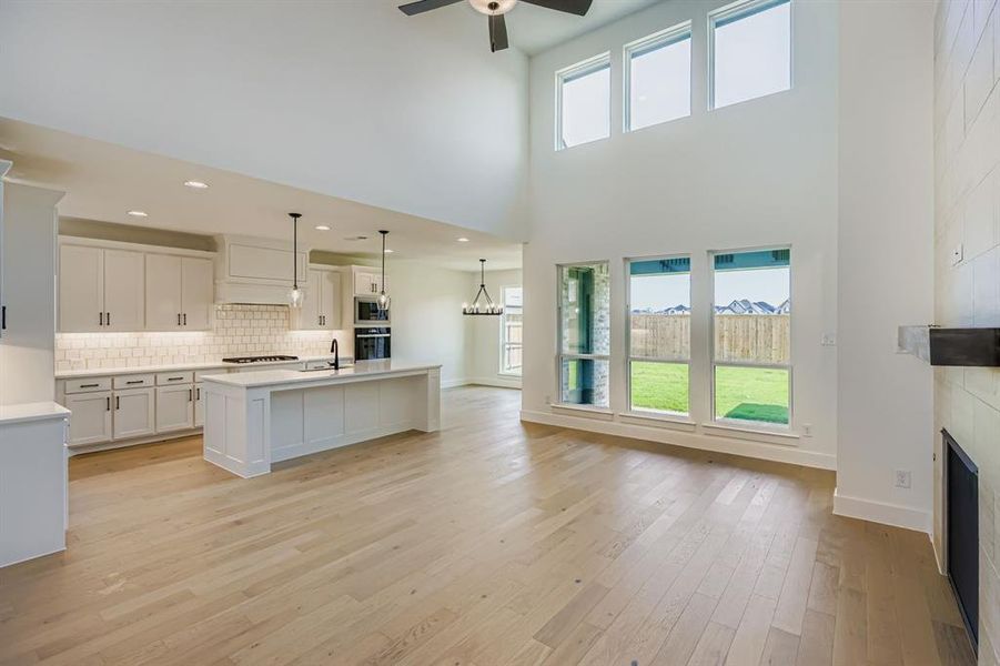 Kitchen featuring white cabinets, healthy amount of natural light, a center island with sink, tasteful backsplash, and a high ceiling