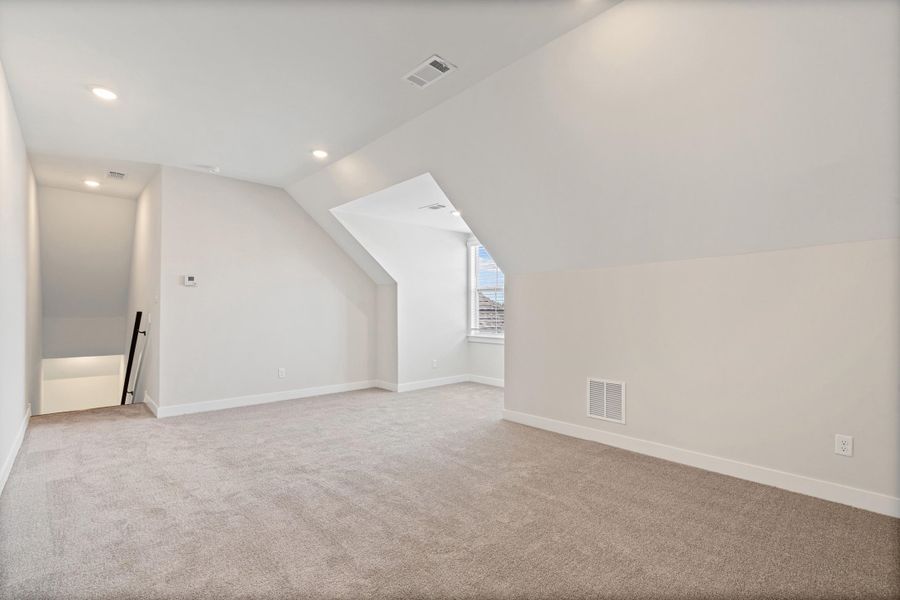 Carpeted room with recessed lighting, sloped ceilings, and a window providing natural light Carpeted room with recessed lighting, sloped ceilings, and a window providing natural light