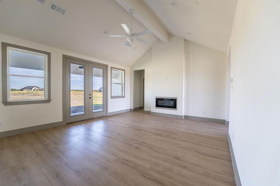 Unfurnished living room featuring light wood-style floors, a glass covered fireplace, beamed ceiling, a ceiling fan, and high vaulted ceiling Unfurnished living room featuring light wood-style floors, a glass covered fireplace, beamed ceiling, a ceiling fan, and high vaulted ceiling