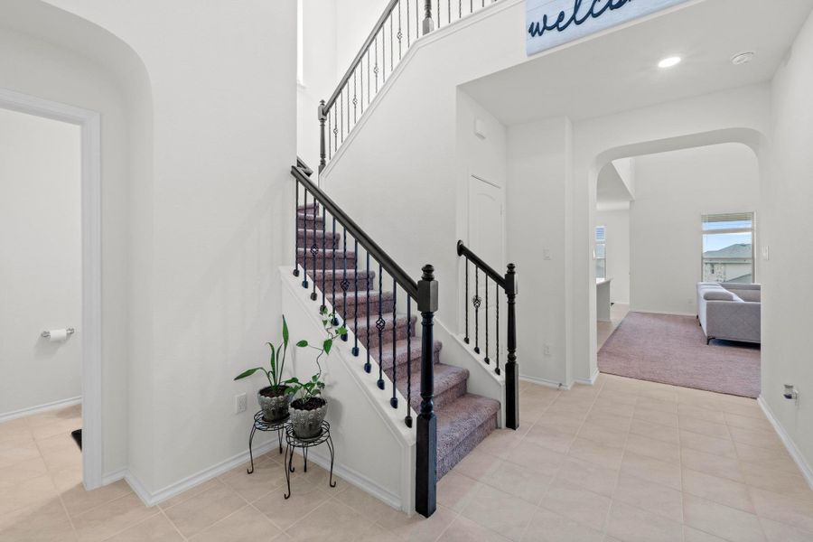Foyer featuring a grand staircase with dark wood newel posts and wrought iron balusters, light-toned tile flooring, and a broad arched entryway