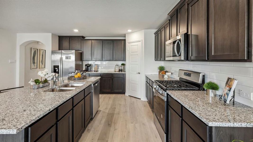 The kitchen features dark wood cabinetry, light granite countertops, stainless steel appliances, and light wood flooring