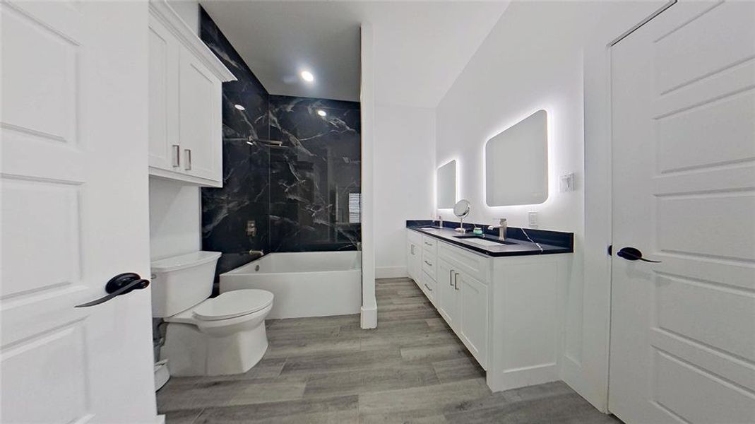 Bathroom featuring a dual vanity with undermount sinks, illuminated mirrors, and a dark countertop Bathroom featuring a dual vanity with undermount sinks, illuminated mirrors, and a dark countertop