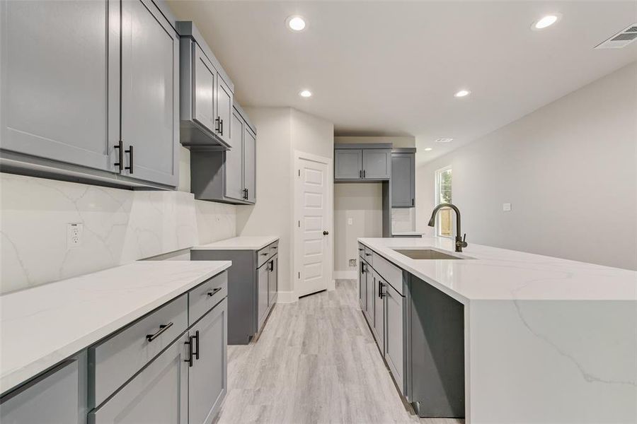 Kitchen with gray cabinetry, light stone countertops, recessed lighting, backsplash, and light wood finished floors Kitchen with gray cabinetry, light stone countertops, recessed lighting, backsplash, and light wood finished floors
