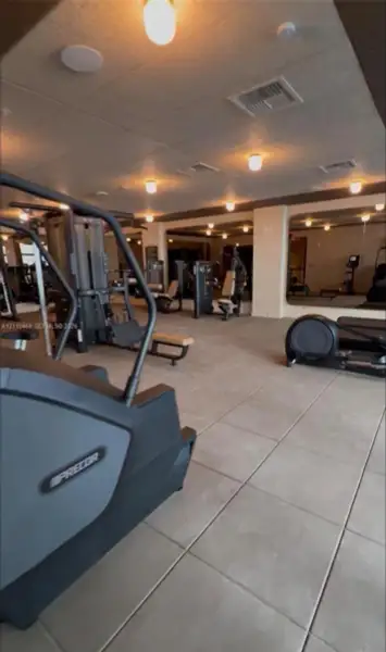 Large-scale exercise facility featuring expansive mirrored wall panels, neutral oversized floor tiling, and recessed ceiling lighting