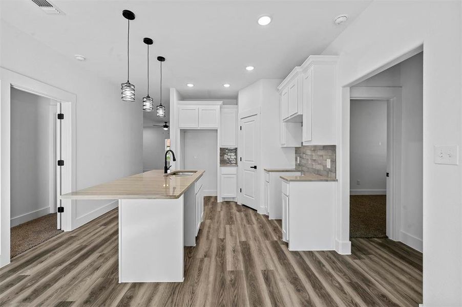 Kitchen with tasteful backsplash, sink, a center island with sink, white cabinets, and hanging light fixtures