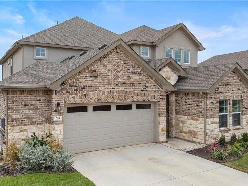 French country inspired facade featuring stone siding, a shingled roof, and driveway