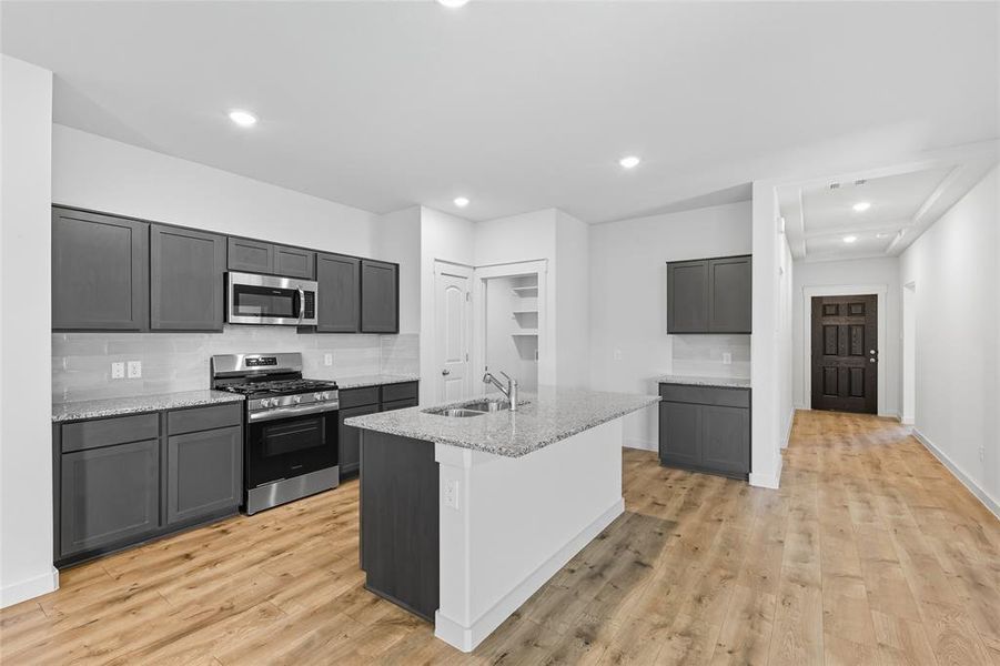Kitchen featuring tasteful backsplash, stainless steel appliances, recessed lighting, light stone countertops, and light wood finished floors