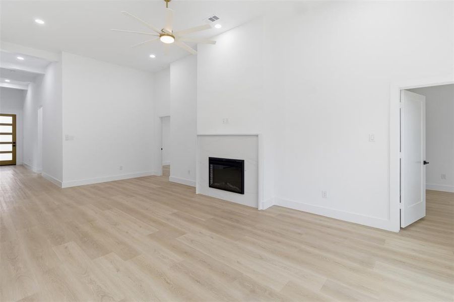 Unfurnished living room with light wood finished floors, ceiling fan, recessed lighting, a glass covered fireplace, and a towering ceiling