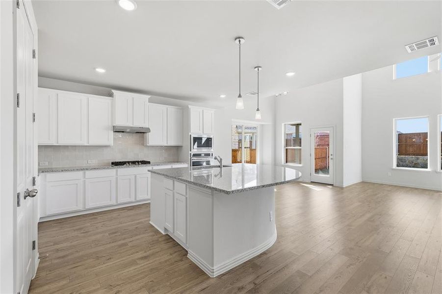 Kitchen with white cabinetry, a kitchen island with sink, light stone counters, decorative light fixtures, and recessed lighting