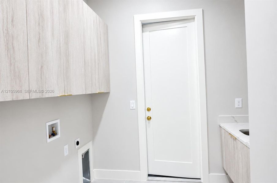 Wall-mounted wood-finish cabinetry, solid-core shaker-style door with brass hardware, stone-surface countertop, and built-in basin