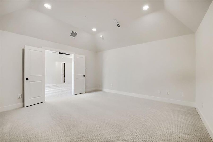 Spacious room with vaulted ceilings, recessed lighting, double doors, and light-toned carpeting Spacious room with vaulted ceilings, recessed lighting, double doors, and light-toned carpeting