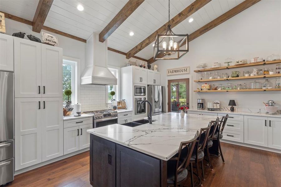 Expansive farmhouse-style kitchen featuring soaring beamed ceilings, a statement island with quartz countertops, and a gas range with convection oven—designed for both everyday cooking and effortless entertaining.