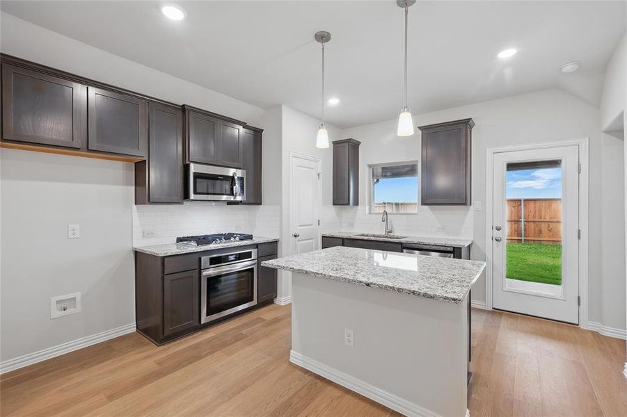 Kitchen featuring pendant lighting, appliances with stainless steel finishes, tasteful backsplash, light stone counters, and recessed lighting