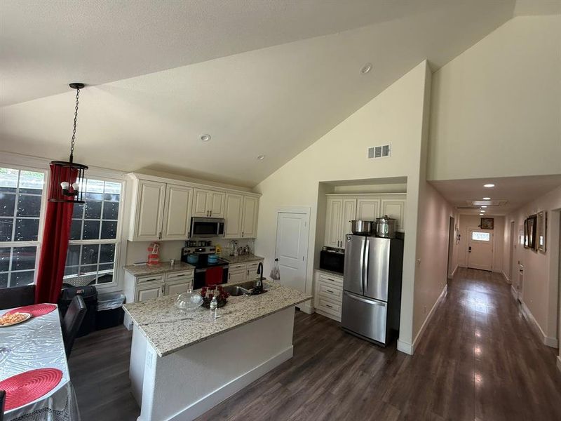 Kitchen featuring appliances with stainless steel finishes, high vaulted ceiling, dark wood-type flooring, light stone counters, and hanging light fixtures