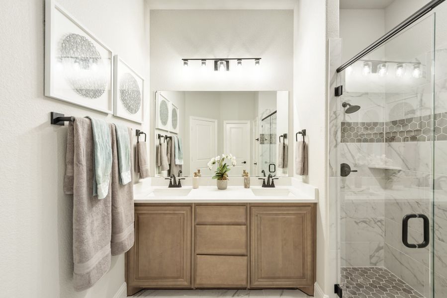 Bathroom with double sink vanity, wood cabinets, large mirror, and glass-enclosed marble tile shower