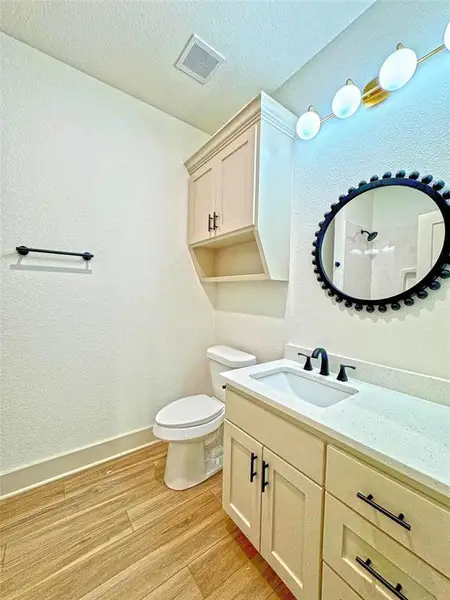 Full bath featuring light wood-style flooring, a textured wall, vanity, a shower, and a textured ceiling