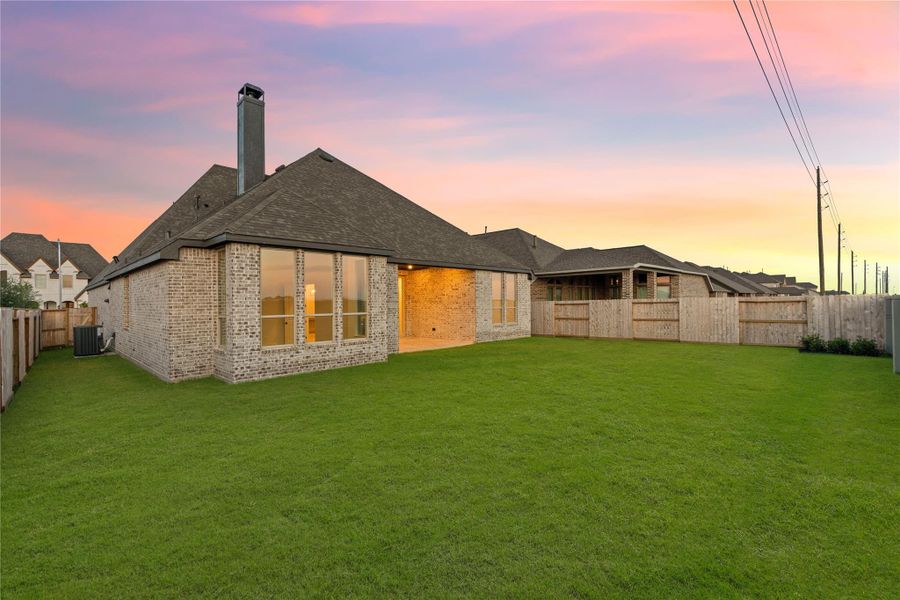 Back of house at dusk with brick siding, a chimney, a fenced backyard, and a shingled roof