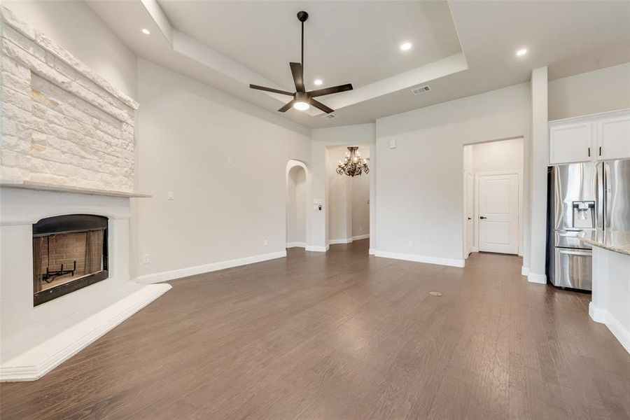 Unfurnished living room featuring a tray ceiling, dark wood-style floors, a fireplace with raised hearth, recessed lighting, and arched walkways Unfurnished living room featuring a tray ceiling, dark wood-style floors, a fireplace with raised hearth, recessed lighting, and arched walkways