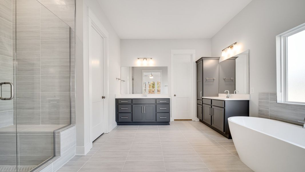 Large tiled bathroom with multiple vanities, glass shower enclosure, and freestanding tub