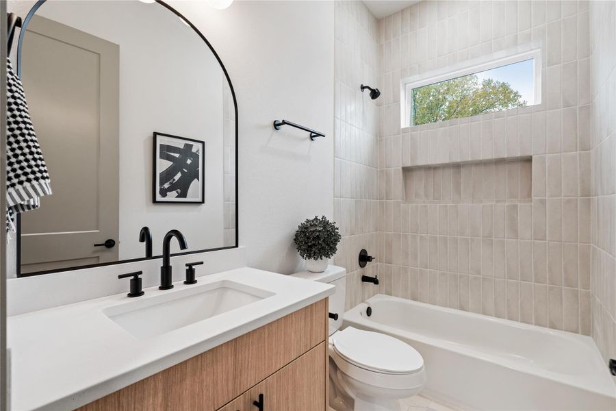 A crisp, modern retreat—this bathroom pairs soft, vertical tilework with bold matte black finishes and warm wood cabinetry. A sleek arched mirror, built-in shower niche, and clerestory window add architectural elegance while filling the space with natural light.