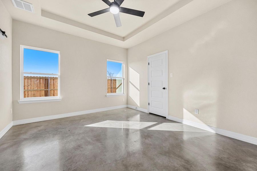 Unfurnished room featuring concrete flooring, ceiling fan, and a tray ceiling