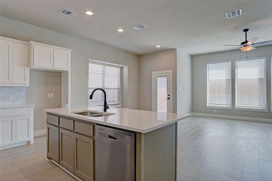 Kitchen with sink, stainless steel dishwasher, an island with sink, ceiling fan, and white cabinets