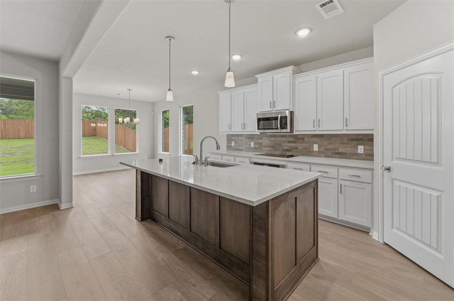 Kitchen featuring a large central island with a light-toned countertop, white cabinetry, a stainless steel microwave, and a tiled backsplash