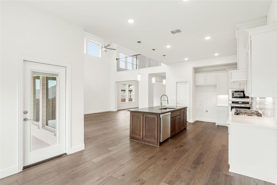 Open-concept kitchen with dark wood island, white cabinets, hardwood floors, and two-story ceiling with upper balcony