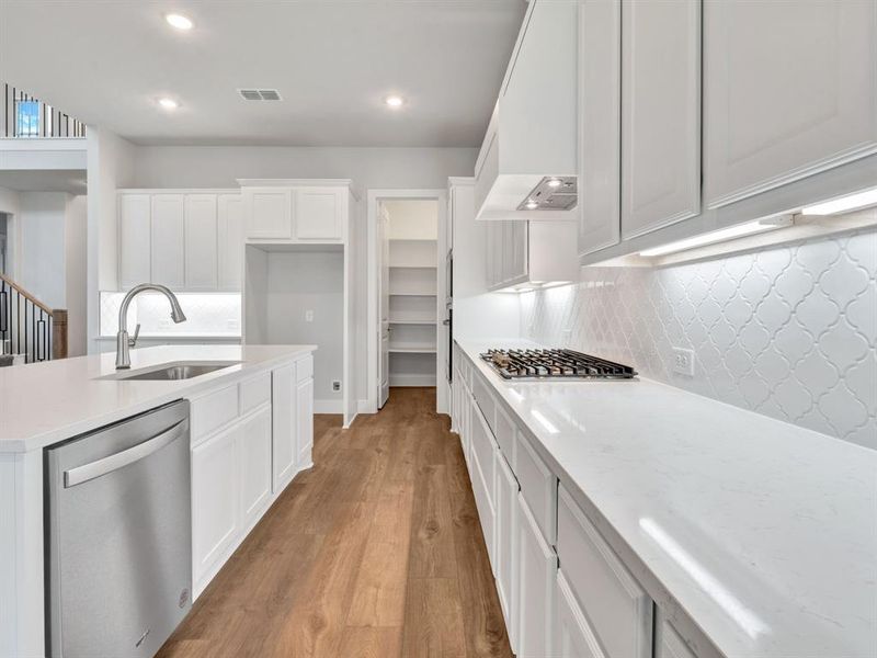 Kitchen with white cabinetry, sink, backsplash, light hardwood / wood-style floors, and appliances with stainless steel finishes