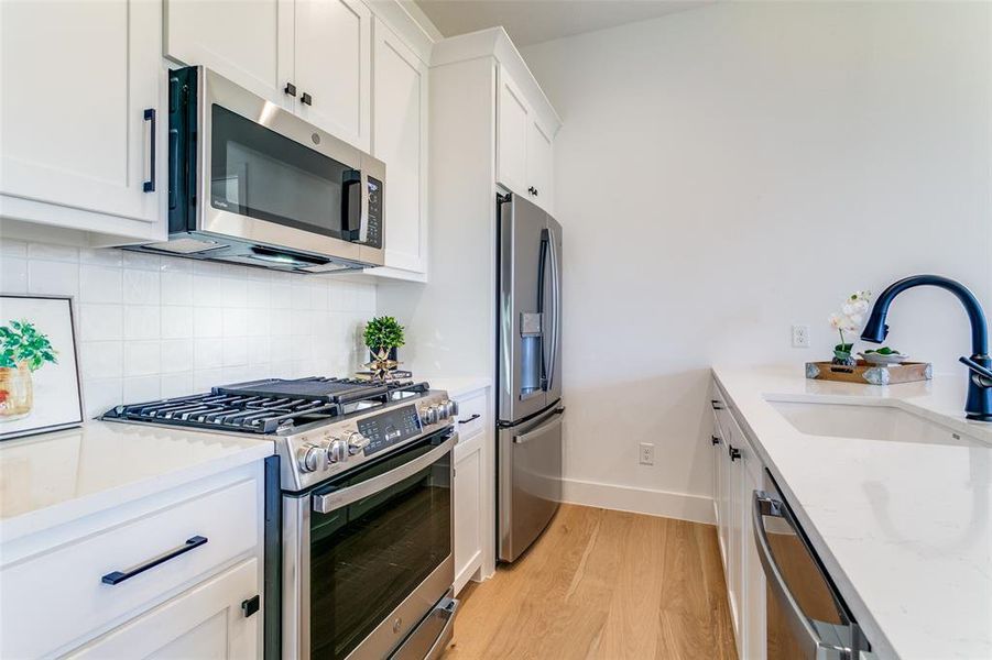 Kitchen with stainless steel appliances, light wood-style flooring, light stone counters, white cabinets, and tasteful backsplash