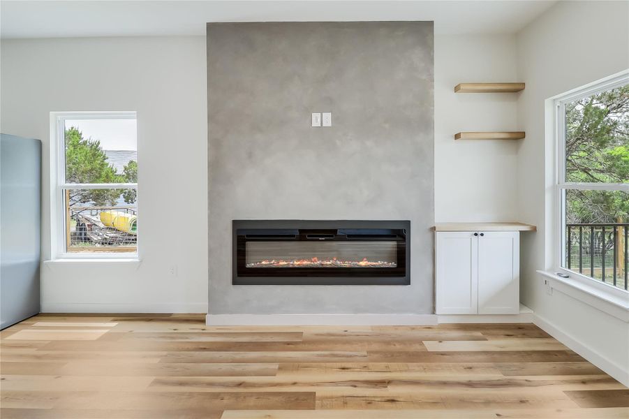 Unfurnished living room featuring a glass covered fireplace, light wood-style flooring, and a wealth of natural light